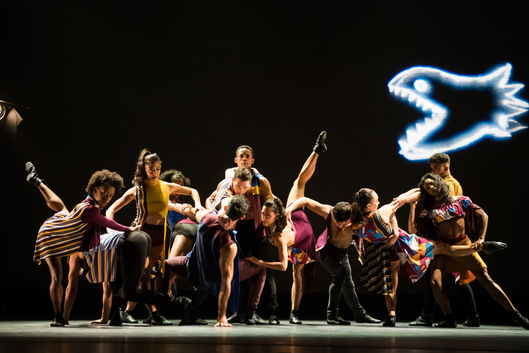 Dancers grouped together on stage in front of a neon sign.